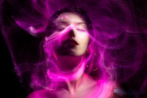 Frau wird mit geschlossenen Augen von violettfarbenen Nebelwolken umweht