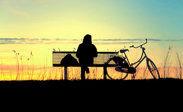 Moment der Achtsamkeit nach untergegangener Sonne, Frau sitzt auf Bank und ruht sich vom Fahrradfahren aus