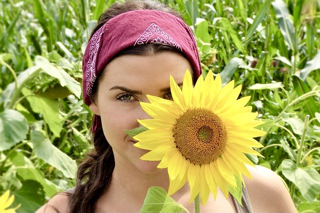 Lust am Leben - Hübsche junge Frau versteckt sich halb hinter Sonnenblume