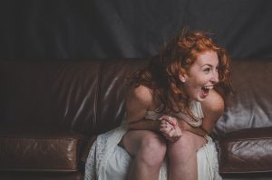 Frau in weißem Kleid auf Sofa lacht schallend